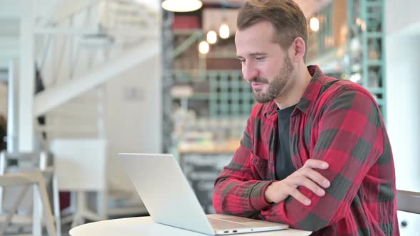 Video Chat on Laptop By Attractive Young Man in Cafe