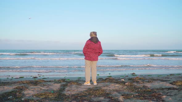 Woman Looks at Rolling Sea Waves Standing on Wet Beach