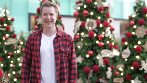 Happy Young Man Smiling Against Illuminated Christmas Trees Outdoors