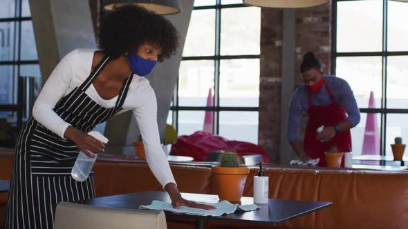 Diverse cafe workers wearing face masks disinfecting tables