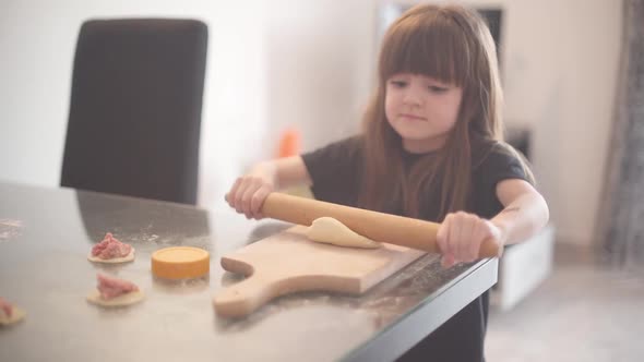 A Little Girl Helps Her Mother in the Kitchen and Kneads the Dough