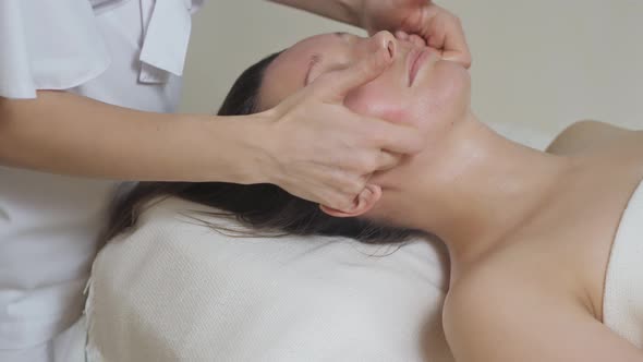 Cute Brunette Woman on Face Massage in Spa Salon