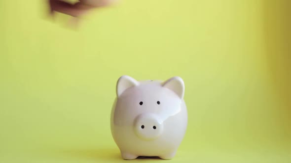 Man Is Putting Coins in Pink Piggy Bank on Yellow Backgroung, Hand Closeup.