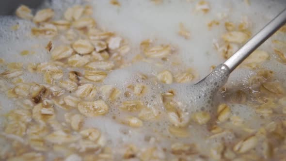 Spoon stirring oatmeal with fresh milk in a gray bowl. Preparing a healthy morning breakfast