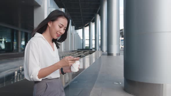 Young Asia businesswoman holding disposable paper cup of hot drink and using smart phone.