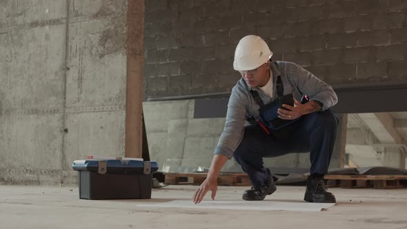 Builder Checking Architectural Papers on Floor