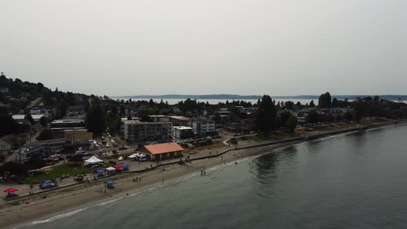 Clockwise drone shot showcasing people relaxing at Alki Beach in the Seattle suburbs. This 4K cinema