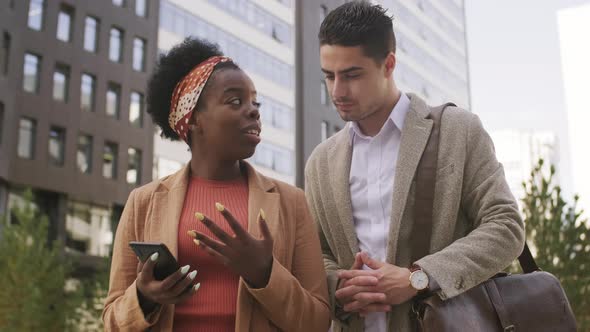  Businesswoman and Businessman Looking at Mobile Phone Outside