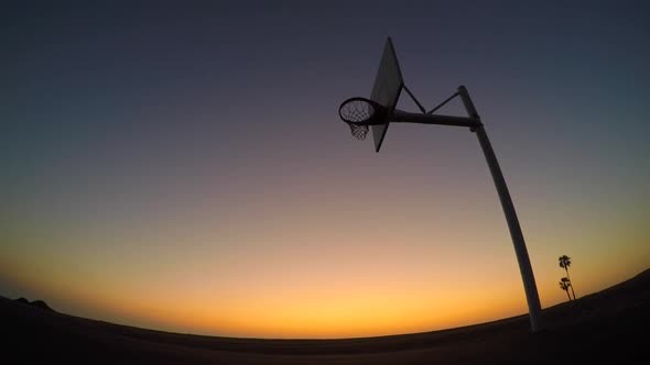 Silhouette of a young man playing street basketball on the beach at sunset.