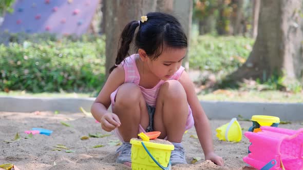 Two cute little sisters are having fun playing outdoors with plastic toys sitting in the sandbox.