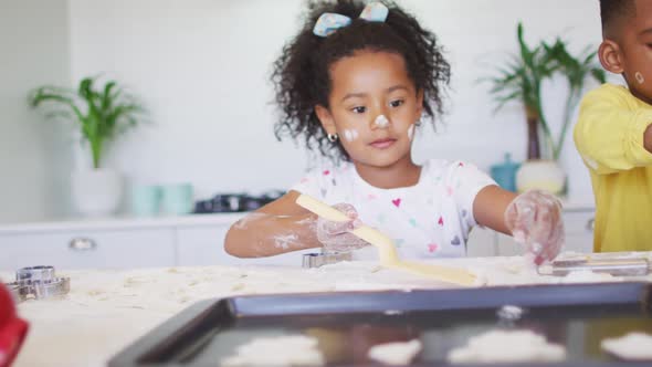 Happy, messy african american siblings making cookies together in kitchen