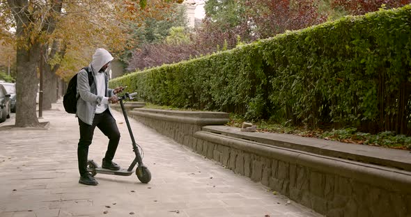 Black Man Standing on an Electric Scooter with a Phone
