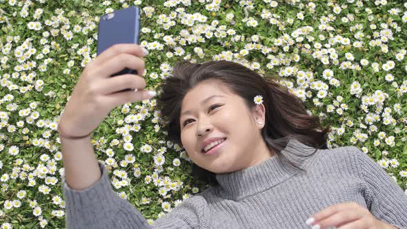 Happy asian girl taking a selfie with a daisy between her hair and daisies co
