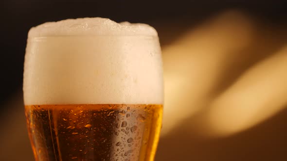 Closeup of Rotating Fresh Beer with Abstract Golden Background and Drops on Glass