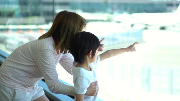 Asian Mother And Her Son Looking Through Window At Airport