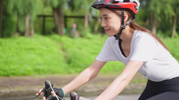 Asian young sport woman wear helmet, exercise by riding bicycle in the evening in public park.