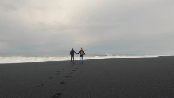 Young Hipster Couple Running on Volcanic Black Sand Beach in Iceland and Having Fun at Sunset Slow