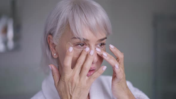 Closeup Middle Aged Woman with Grey Hair and Brown Eyes Applying Eye Patches in Slow Motion Standing