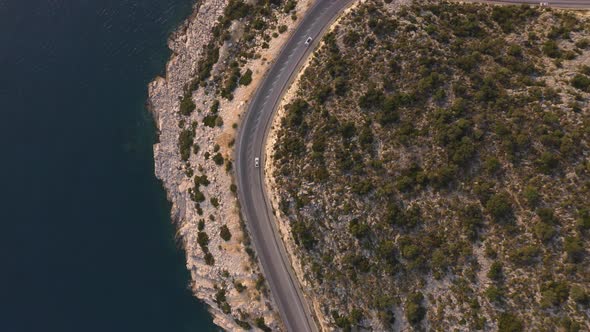 Aerial View From Drone of Cars Going Through Mountain Road Above Rocky Coast