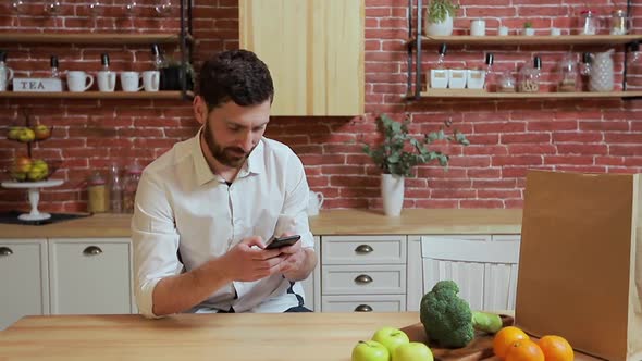 Man Browsing on Mobile Phone at Home Kitchen. Handsome Young Man Browsing on Smartphone Smiling