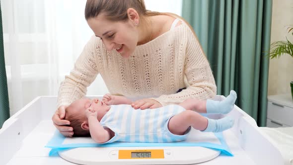 Smiling Mother Looking and Stroking Her Little Son While Weighing Him on Digital Scales on Changing