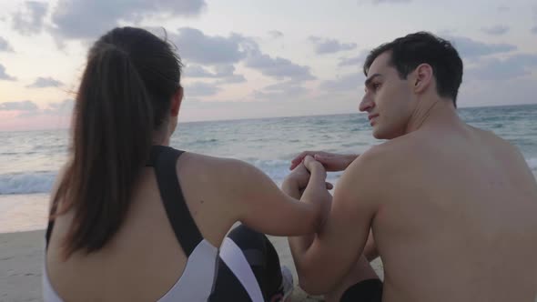 Attractive fitness couple chill out on beach at sunset. Rest after workout
