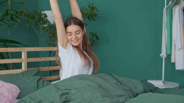 A Happy Young Woman Wakes Up in a Happy Mood Stretching Cheerfully in Bed