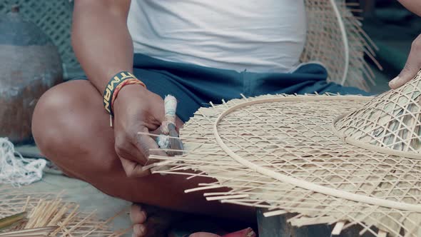 Man cutting surplus of bamboo reed on a handcrafted hat with scissors. Process of making handcrafted