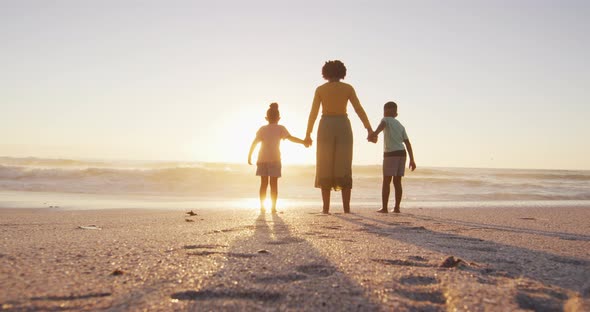 African american mother with children jumping and holding hands on sunny beach