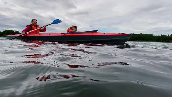 Woman Rows Sports Kayak with Daughter Along Lake Water