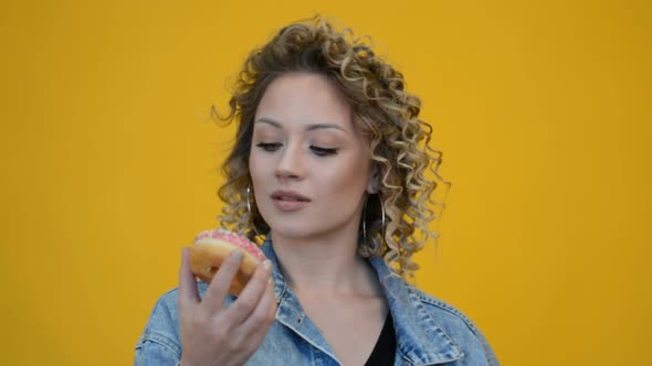 Portrait of a Curly Girl on a Yellow Background with a Delicious Donut in Her Hands