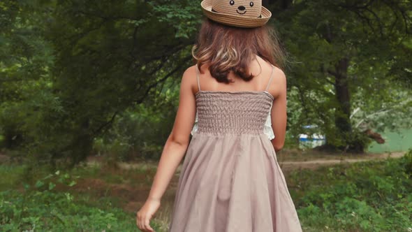 Back view of little girl in a straw hat and dress walking in the park