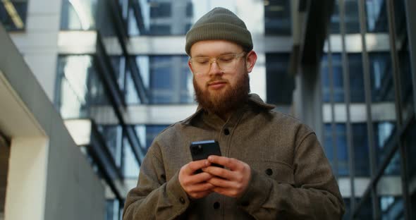 A Young Man is Typing on a Mobile Phone While Walking Around the Business Center