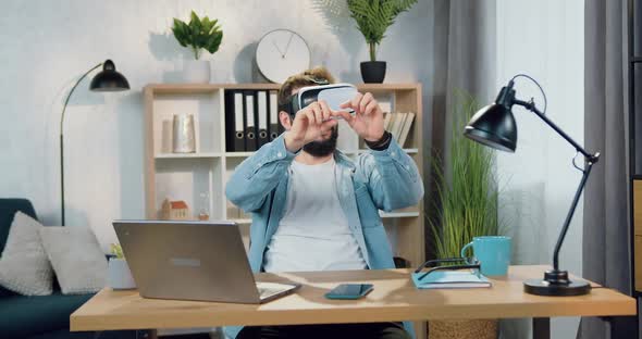 Bearded Worker in Virtual Reality Headset Sitting at His Workplace and Working on Imaginary Screen