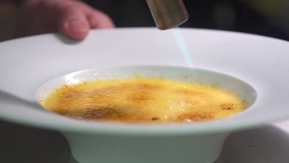 Close-up of a chef cook preparing a creme brulee dessert dining in a restaurant.