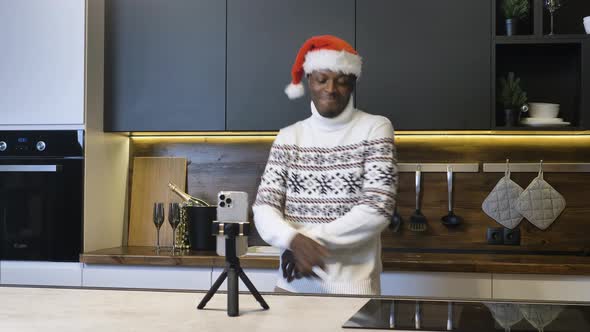 Happy African American Man in Christmas Hat Dancing Energetically in the Kitchen in Front of