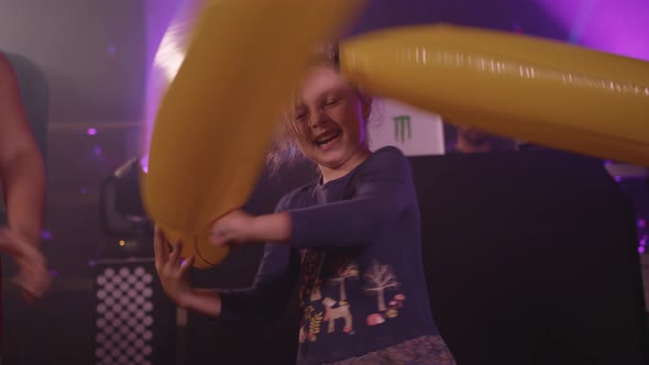 Young Girls Happily Play Fight with Inflatable Bananas at Children's Disco / Party