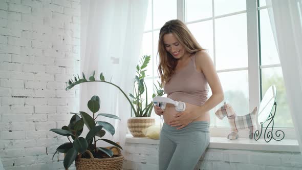 Close Up Cheerful Pregnant Mother Puting Headphone on Tummy at Home.