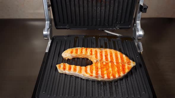 The Grill Lid Opens. A Piece Of Salmon Fish Is Cooking On The Electric Grill