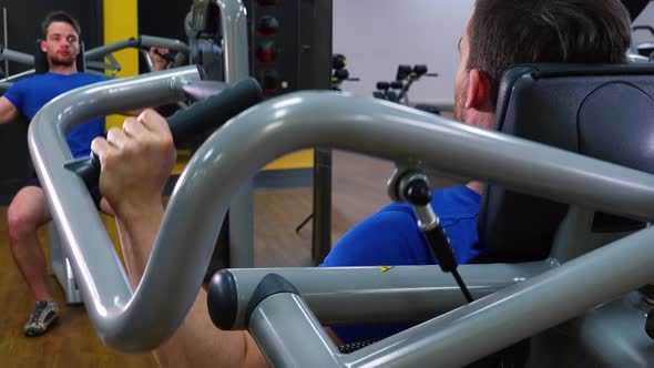 A Young Fit Man Trains on a Machine in a Gym - Closeup From Behind