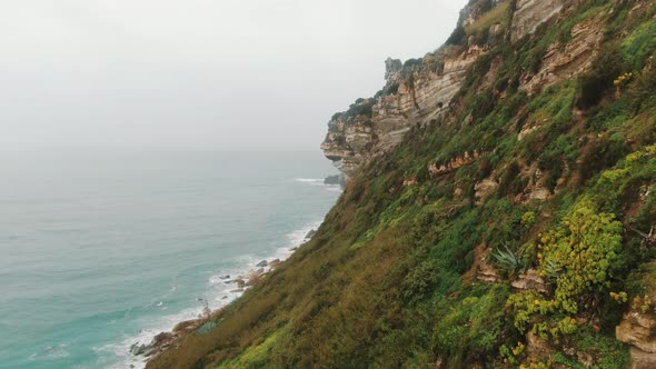 Rocky Mountain Rises Over Tranquil Ocean Disappearing in Fog