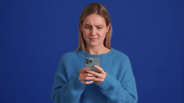 Negatively surprised woman wearing blue sweater texting by phone