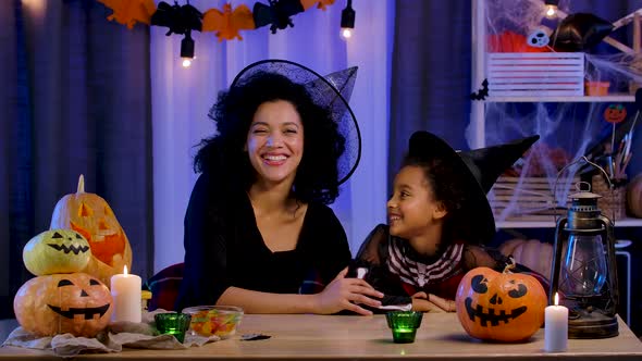 Mom and Daughter African American in Festive Costume and Witch Hat Joyfully Laugh and Have Fun