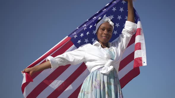 Confident African American Young Woman with USA Flag Posing at Background of Clear Blue Sky
