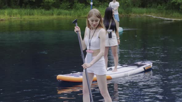 Young Blonde Pretty Woman Standing on the Board on the River and Using the Paddle