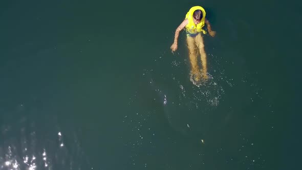 Active kid in life yellow waistcoat swimming alone in the clear water in bright summer day.