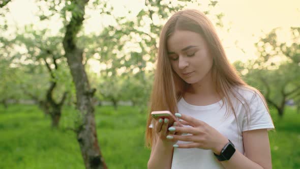 Portrait of a Beautiful Woman Typing on a Mobile Phone in the Park