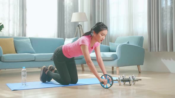 Asian Woman In Sportswear Is Working Out With Exercise Wheel At Home In The Living Room