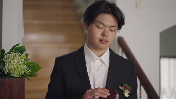 Asian Young Man in Wedding Suit Stretching Ring Box in Hand Smiling Looking Away