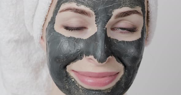 Young Woman with Black Dried Clay Mud Facial Mask on Skin Looking at Camera Smiling and Winking